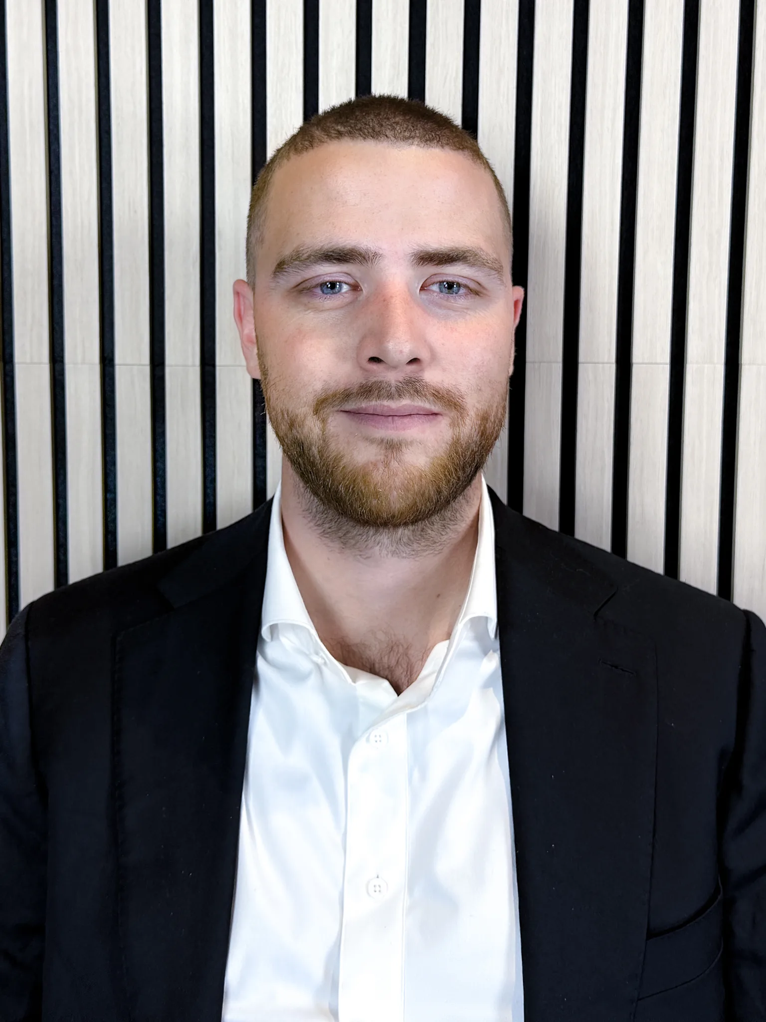 Portrait of Kevin Hanlen, licensed advisor, in a dark navy blazer and open-collared white shirt against a slatted wood wall